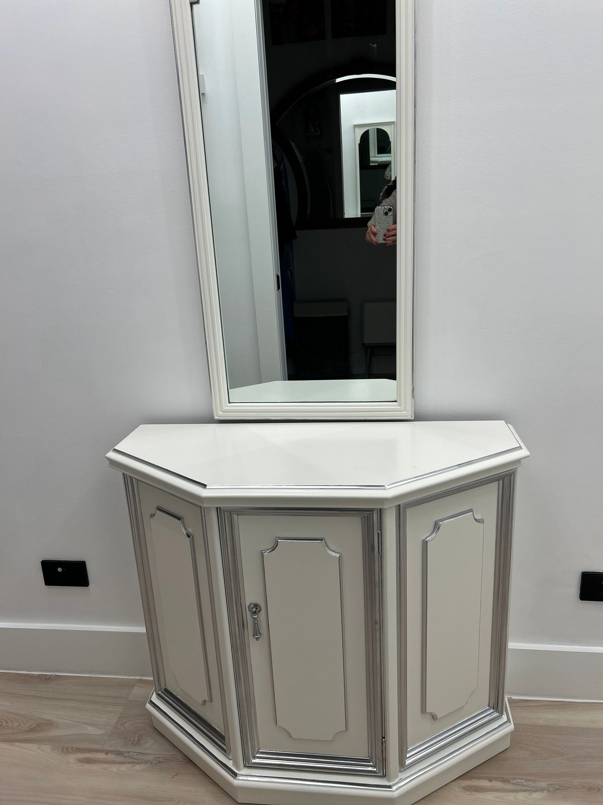 White corner vanity table with mirror against a light gray wall and tiled floor.