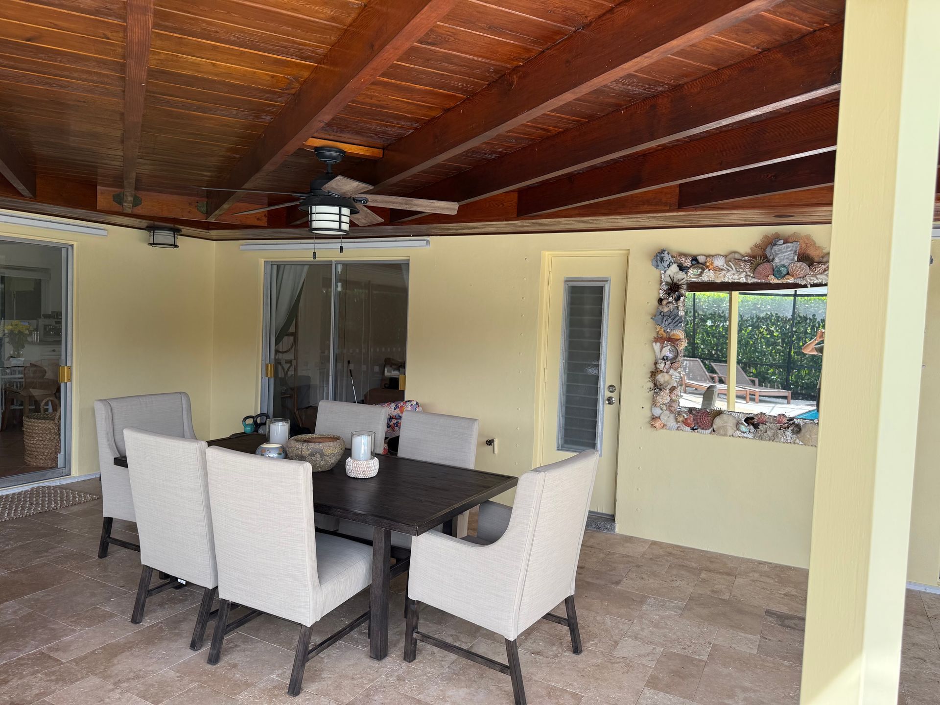 Patio dining area with a dark table, white chairs, tiled floor, and a wooden ceiling with ceiling fan.