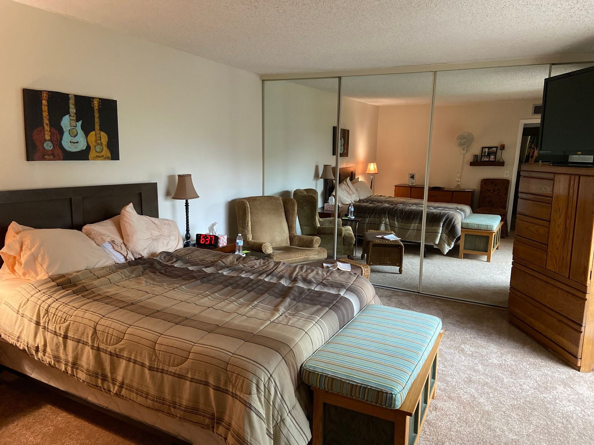 Bedroom with bed, mirrored closet doors, bench, dresser, and warm decor