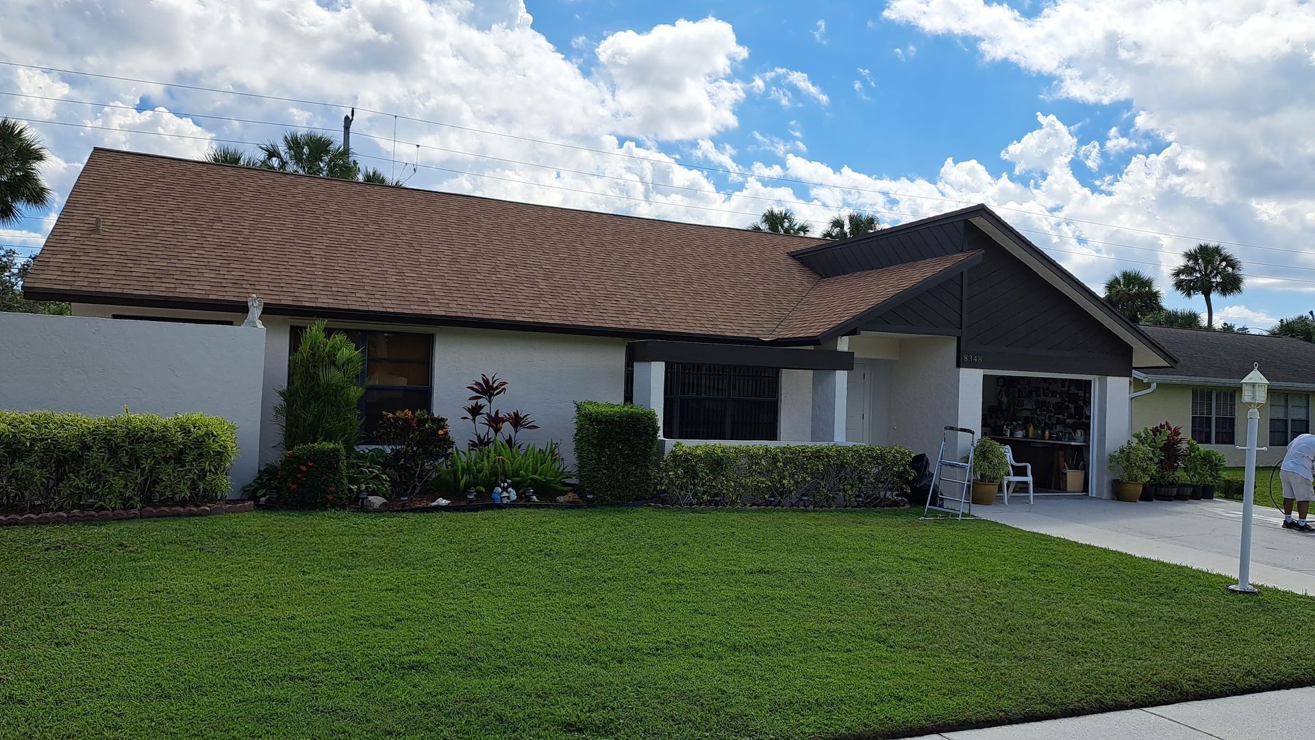 Single-story suburban house with a brown roof, white walls, and a green lawn under a clear sky