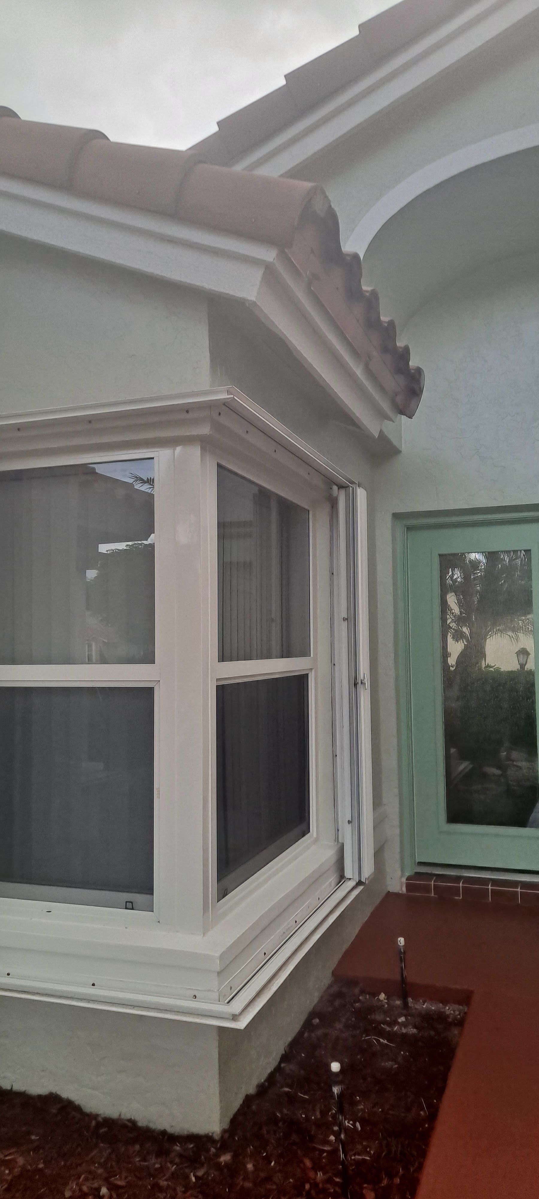 Covered front porch with a white bay window, stucco walls, and a red walkway.
