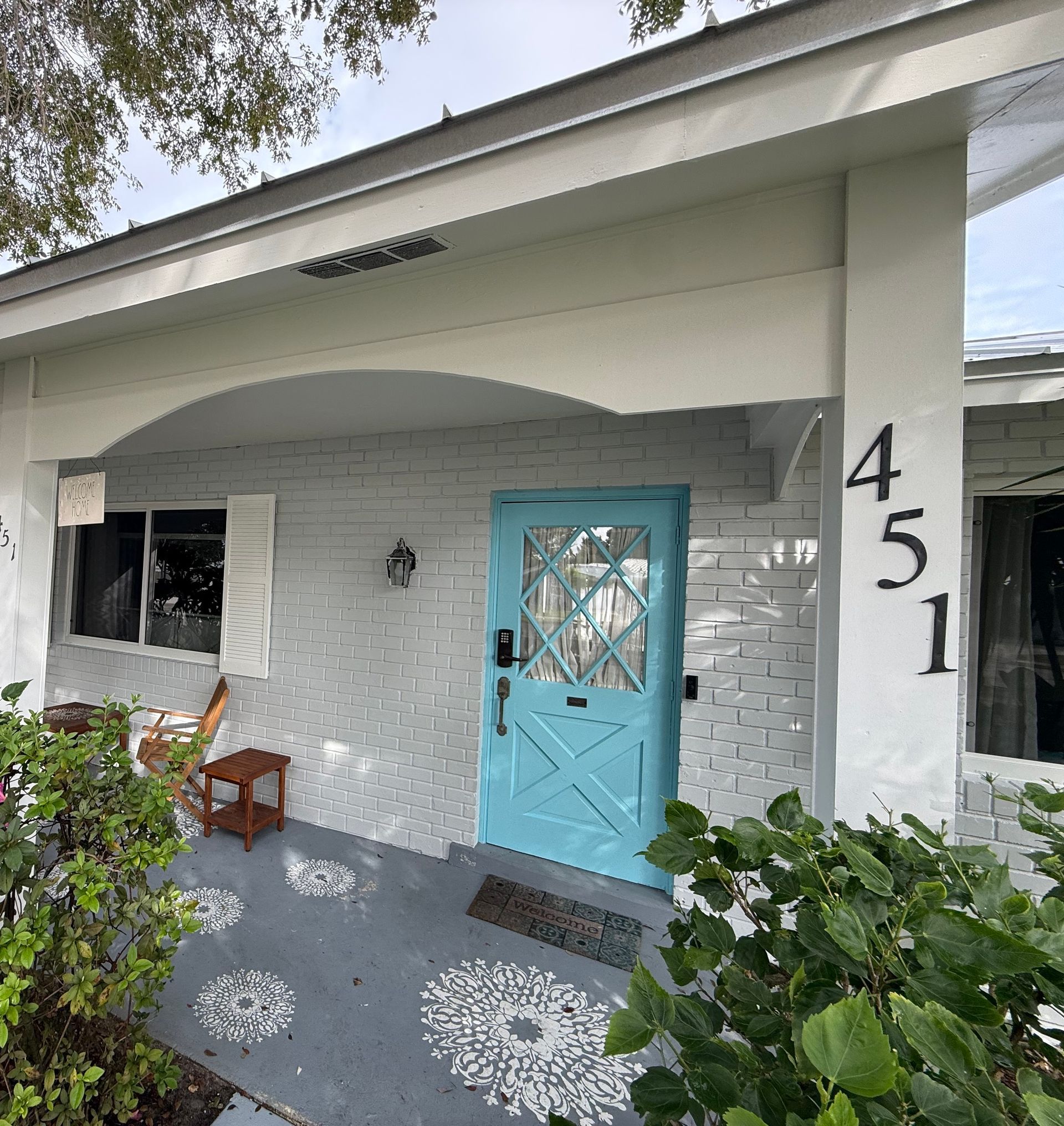 Turquoise front door on a white house with porch plants and the number 451 on the pillar