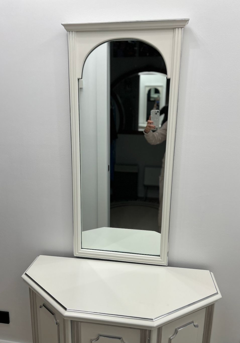 White wall mirror above a white geometric dresser in a room.