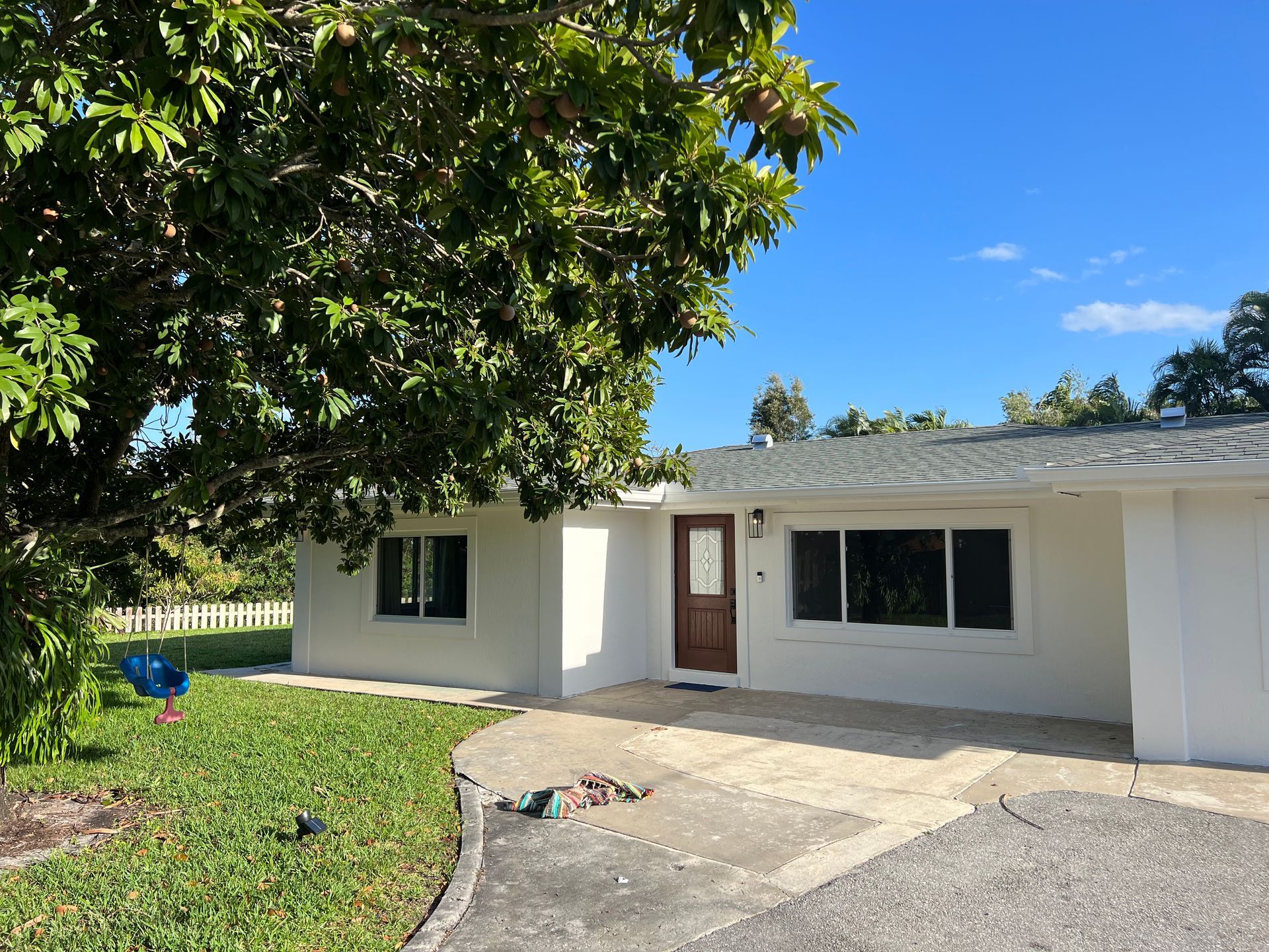 Single-story white house with a brown front door, driveway, and green lawn under a bright blue sky