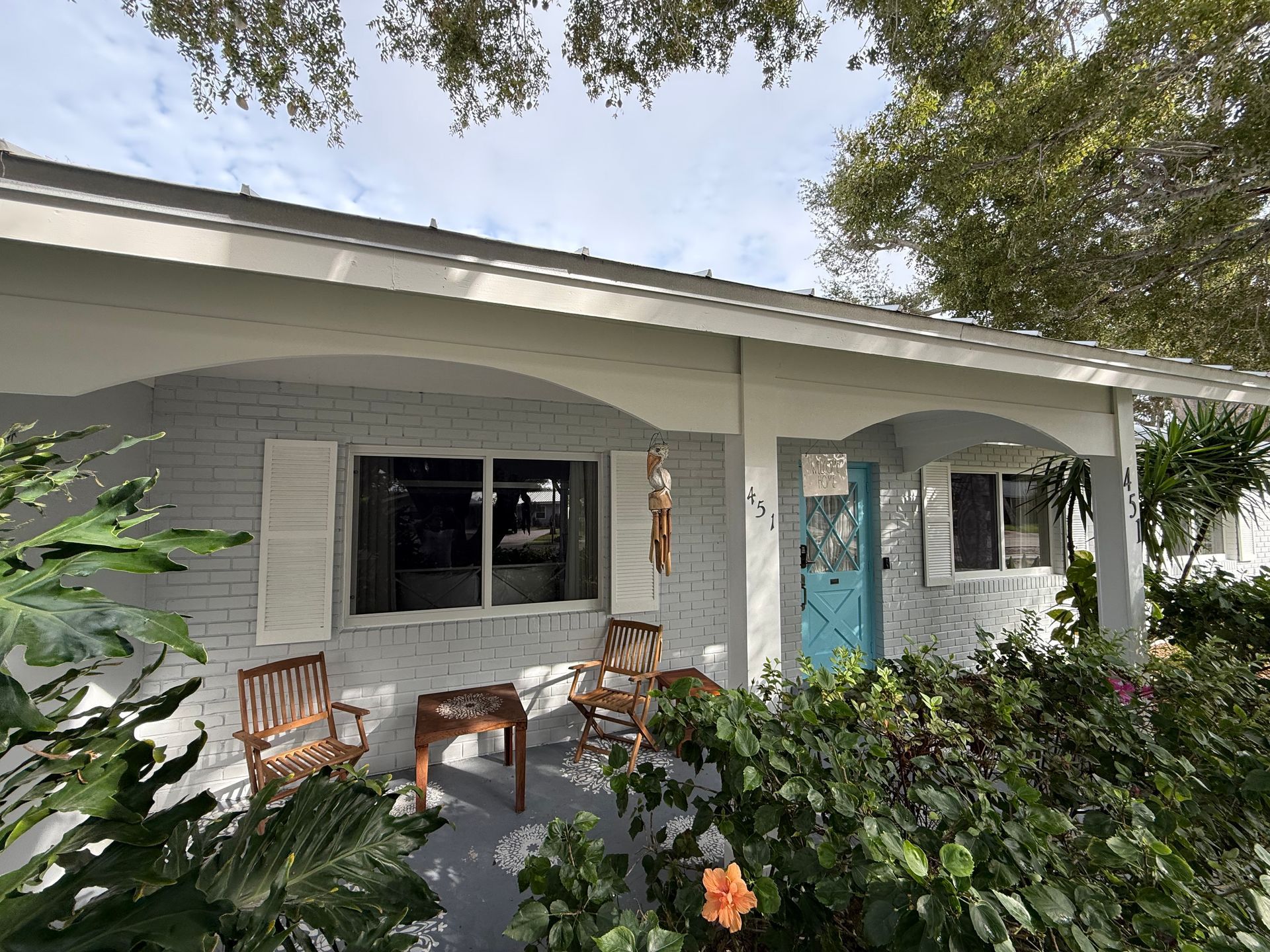 Front porch with white columns, chairs, and lush greenery around a light gray house