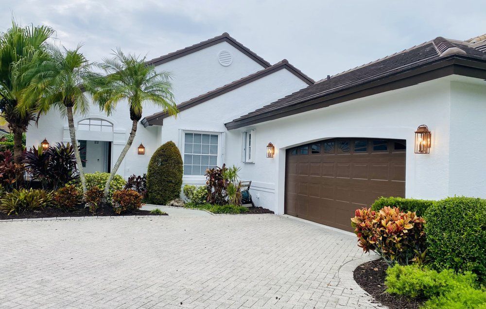Modern white house with brown garage door, palm trees, and a paved driveway