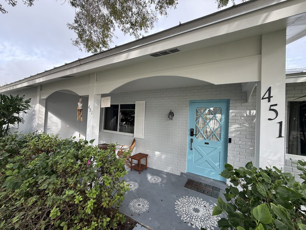 White front porch with blue door, white brick exterior, potted plant, and house number 451.