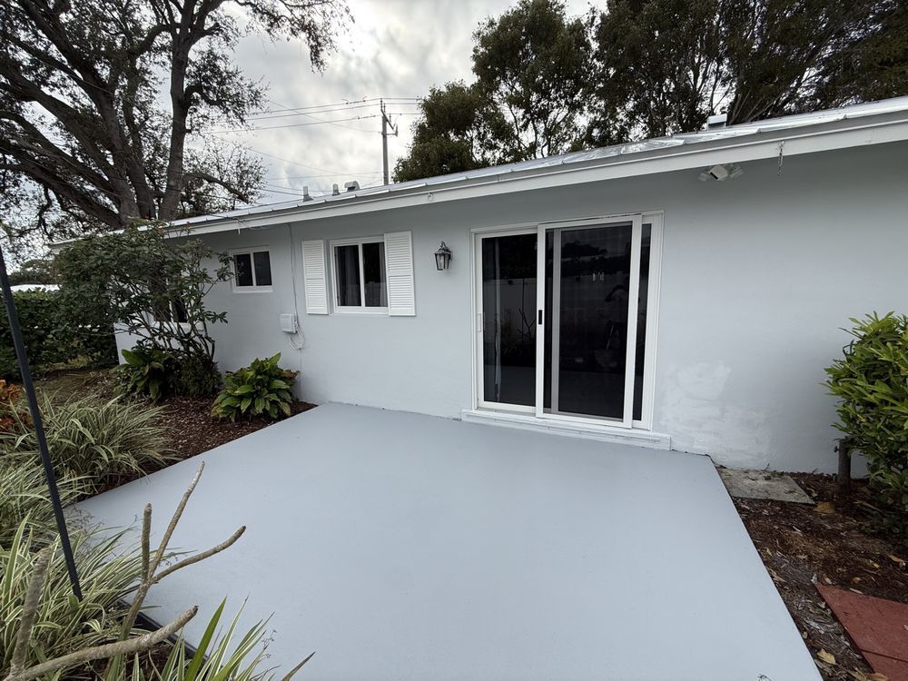 Back patio with gray concrete slab, white house exterior, and sliding glass doors