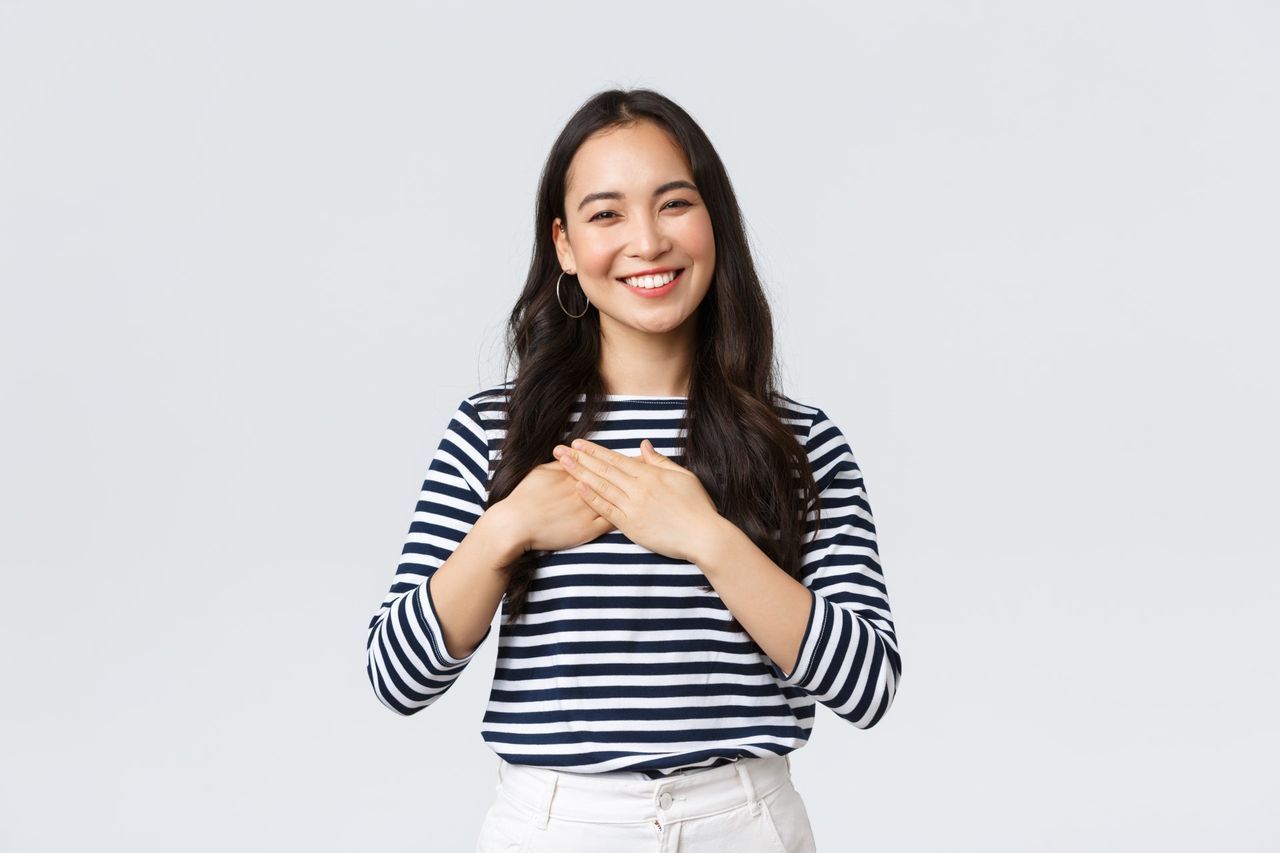 A woman in a striped shirt is smiling and holding her hands on her chest.