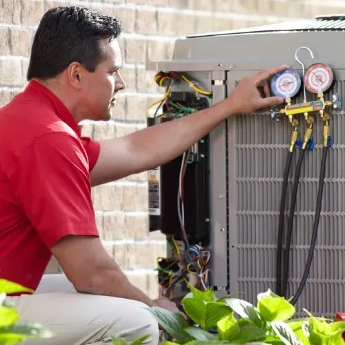 Technician in red shirt inspecting outdoor air conditioning unit with gauges attached
