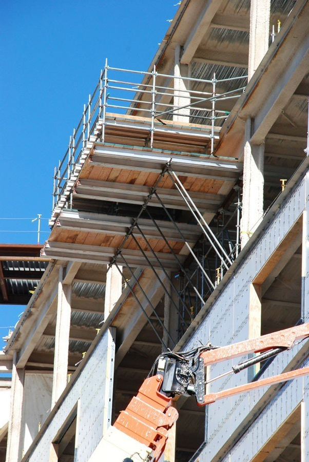 Construction site: scaffolding platform attached to the side of a building under construction. Orange lift below.