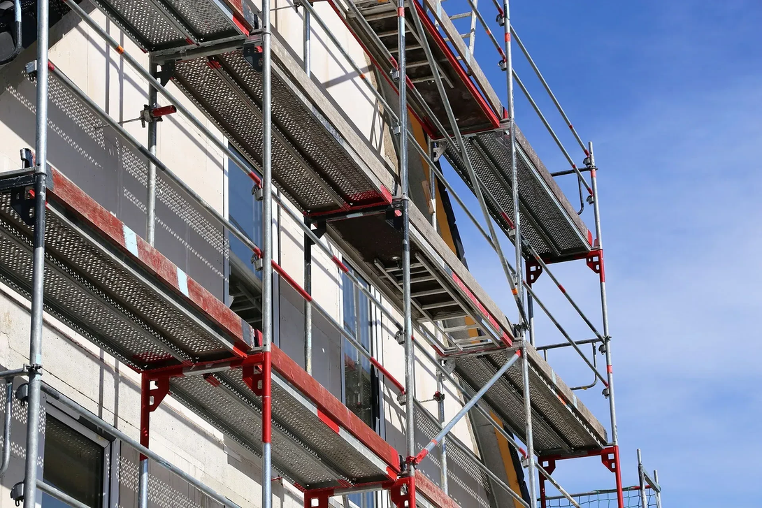 Scaffolding on a building's facade, red and silver metal, against a blue sky.