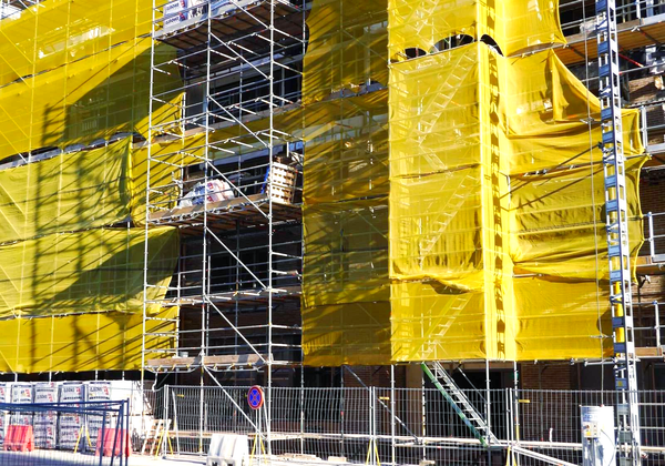 Scaffolding wrapped in yellow netting surrounds a building under construction.