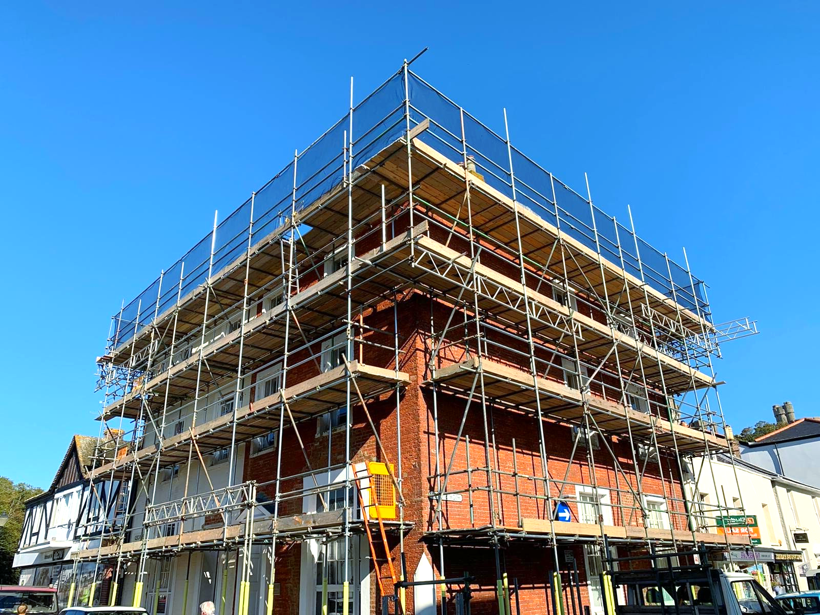 Scaffolding surrounds a three-storey brick and white building under renovation against a clear blue sky.
