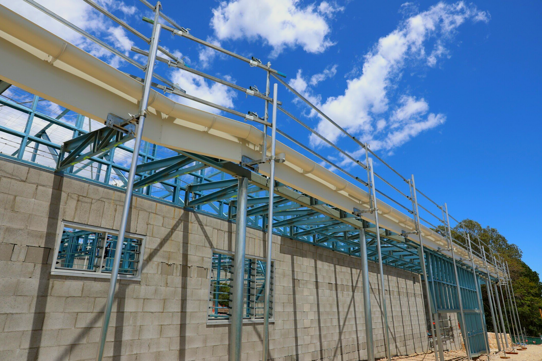 Construction site with a partially built building, steel frame, cinder block walls, and safety railings, against a blue sky.