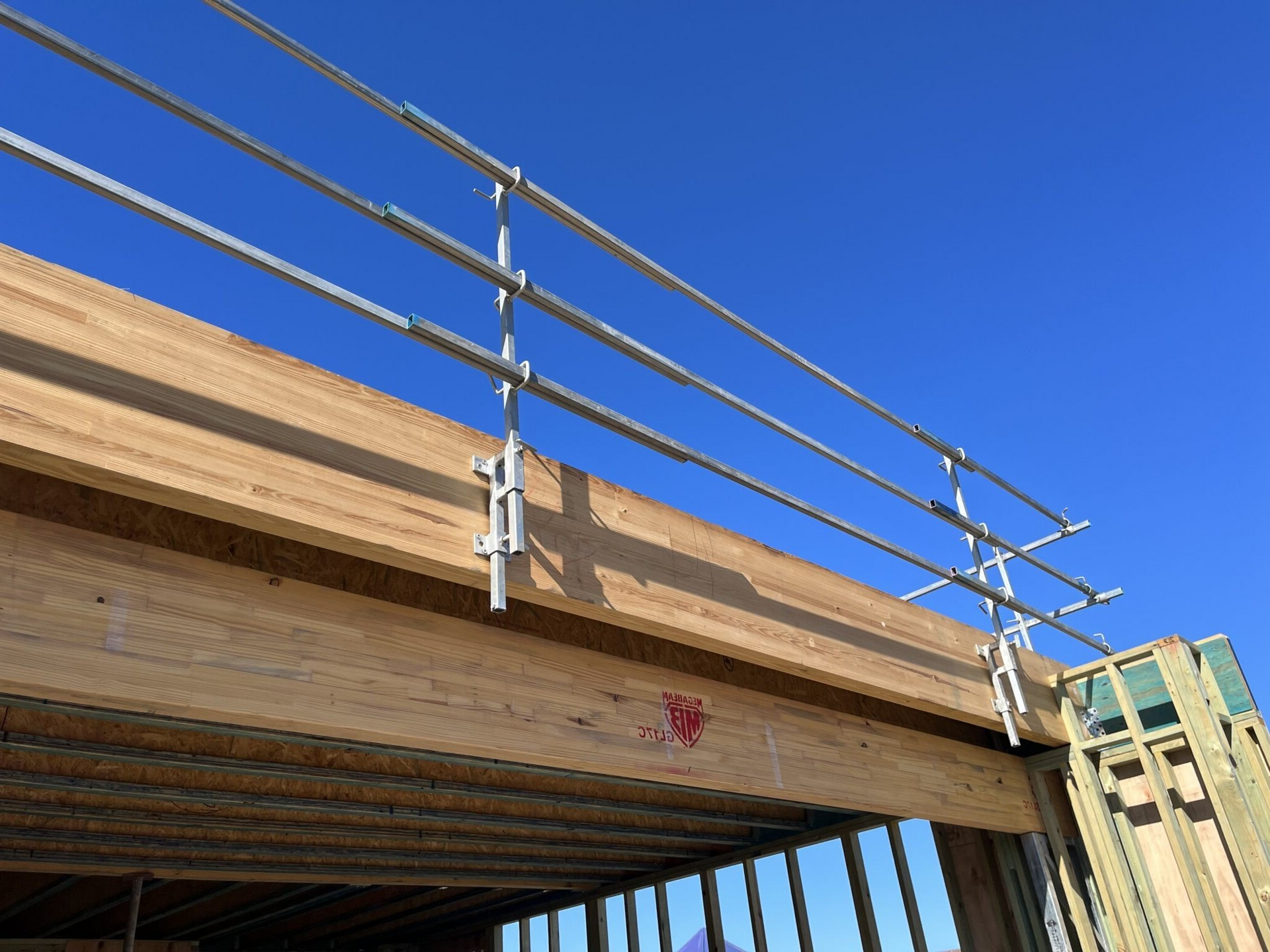 Metal safety railing attached to the edge of a wooden structure, against a bright blue sky.