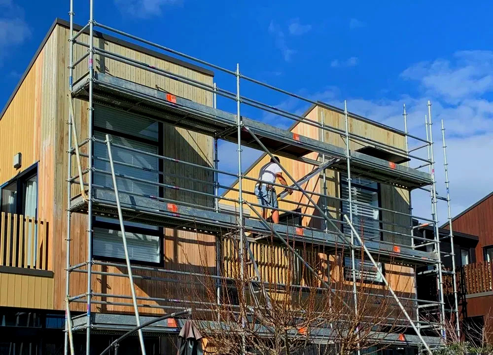 Scaffolding on a two-story building; a worker is on a platform, against a blue sky.