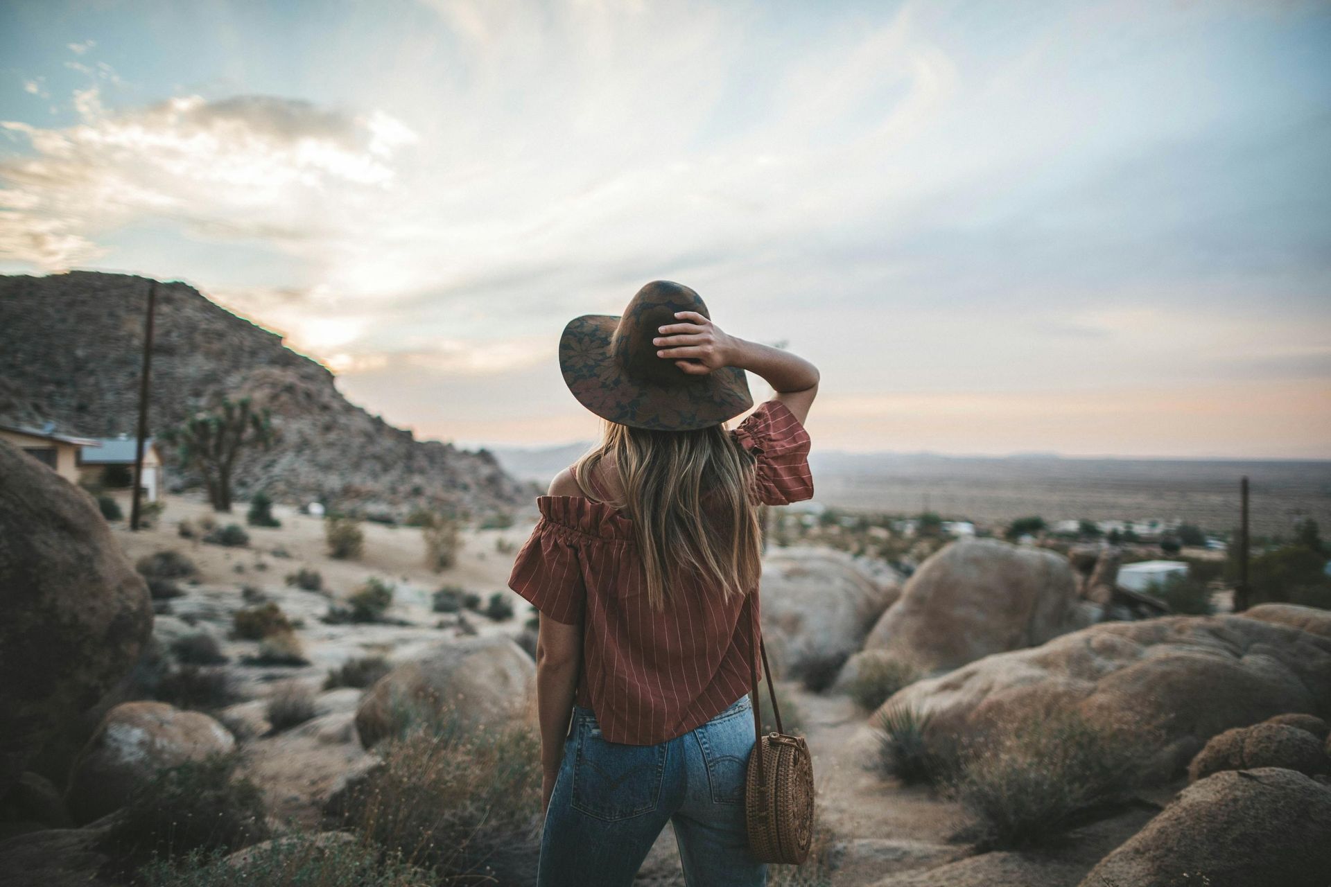 Person sitting on rocks in a desert canyon, facing rugged red cliffs at sunset