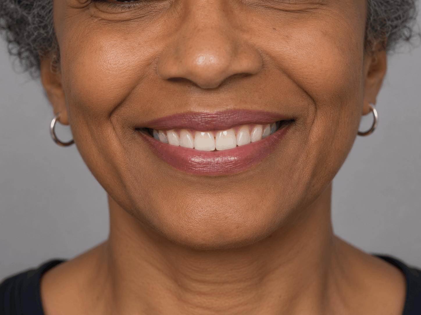 Close-up of a smiling mouth and lower face with hoop earrings on a gray background