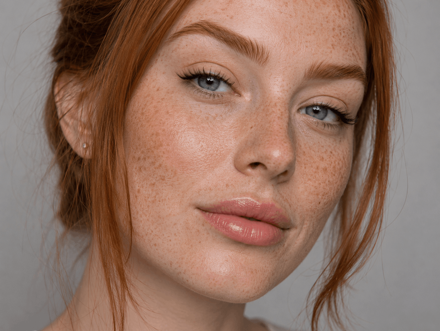 Close-up portrait of a red-haired person with freckles and soft makeup against a gray background