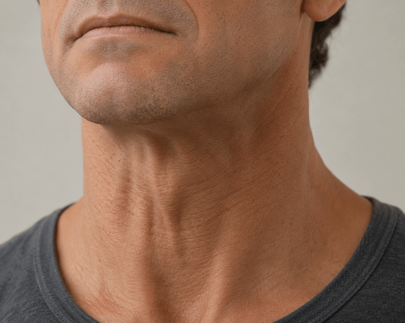 Close-up of a man’s neck and lower face in a dark gray shirt, showing throat muscles and jawline.