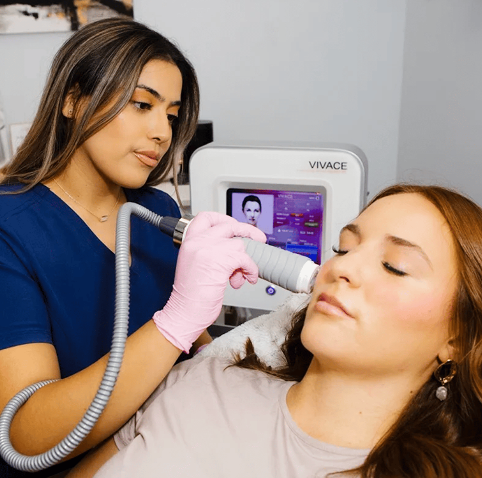 Clinician using a handheld device on a woman’s cheek during a facial treatment in a treatment room