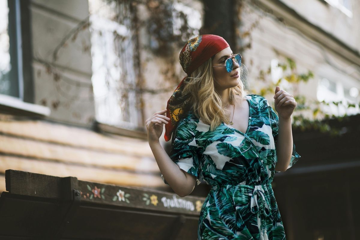 Woman in a red beret and blue sunglasses holding a small flower outdoors near a building