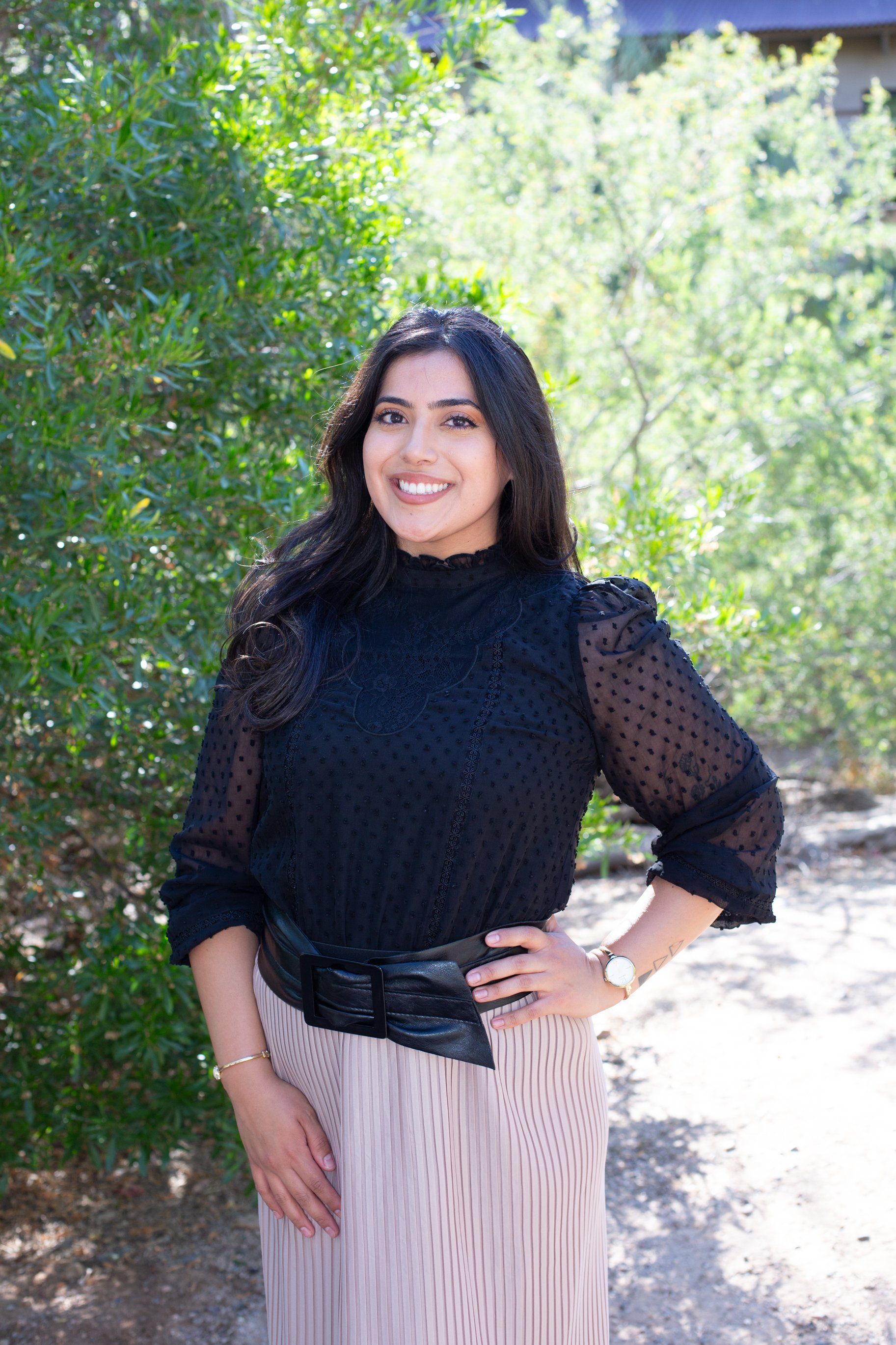 Woman standing outdoors in a black top and patterned skirt, smiling with one hand on her hip.