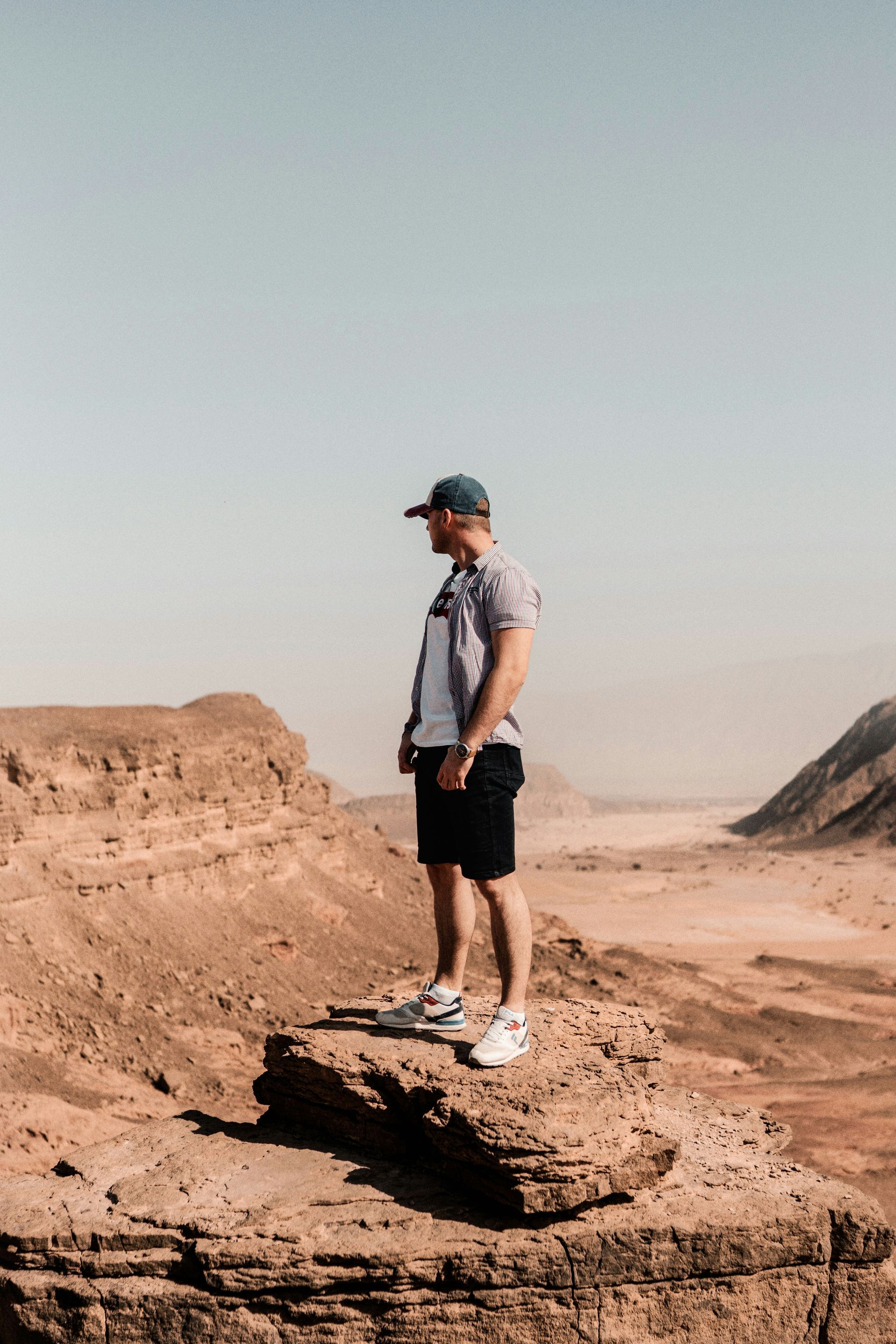 Person standing on a rocky desert outcrop under a clear sky, looking into the distance