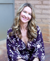 Smiling woman in a purple floral dress sitting against a brick wall