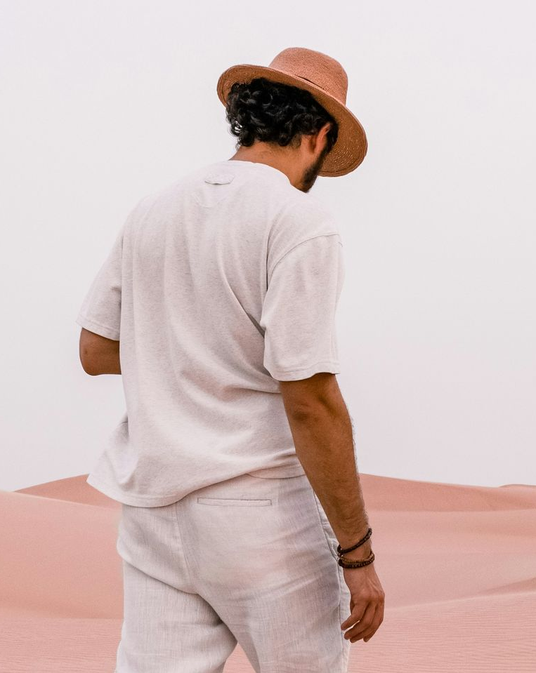 Person in a straw hat and light beige outfit standing against a soft pink backdrop.