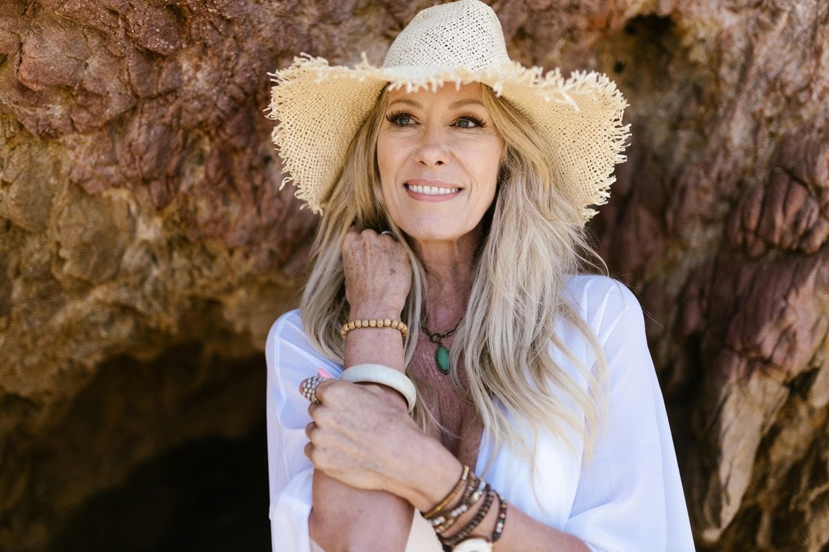Smiling woman in a straw hat and white shirt standing against a rocky backdrop