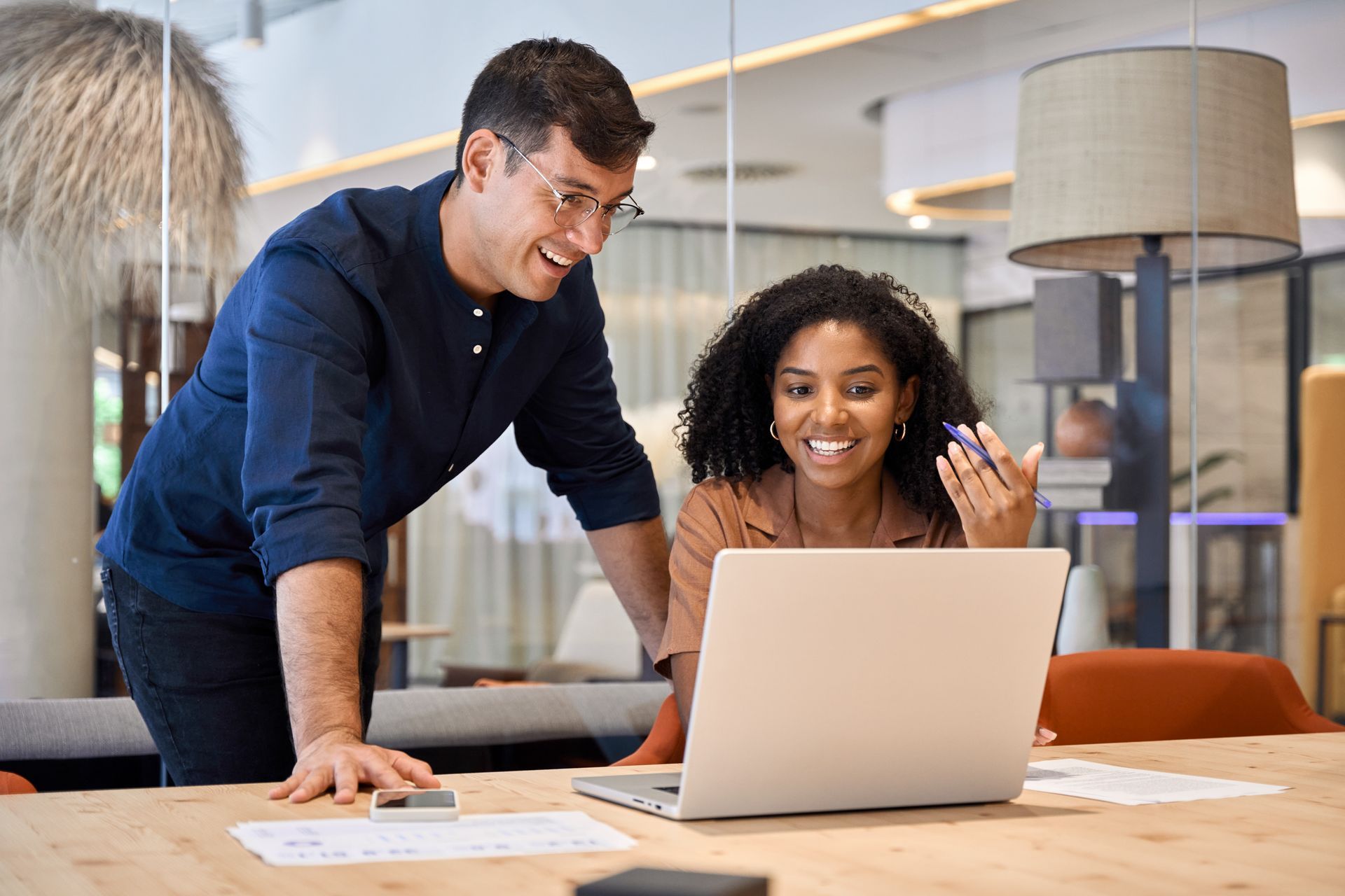 Man and woman looking at laptop, smiling. Inside office, working together.