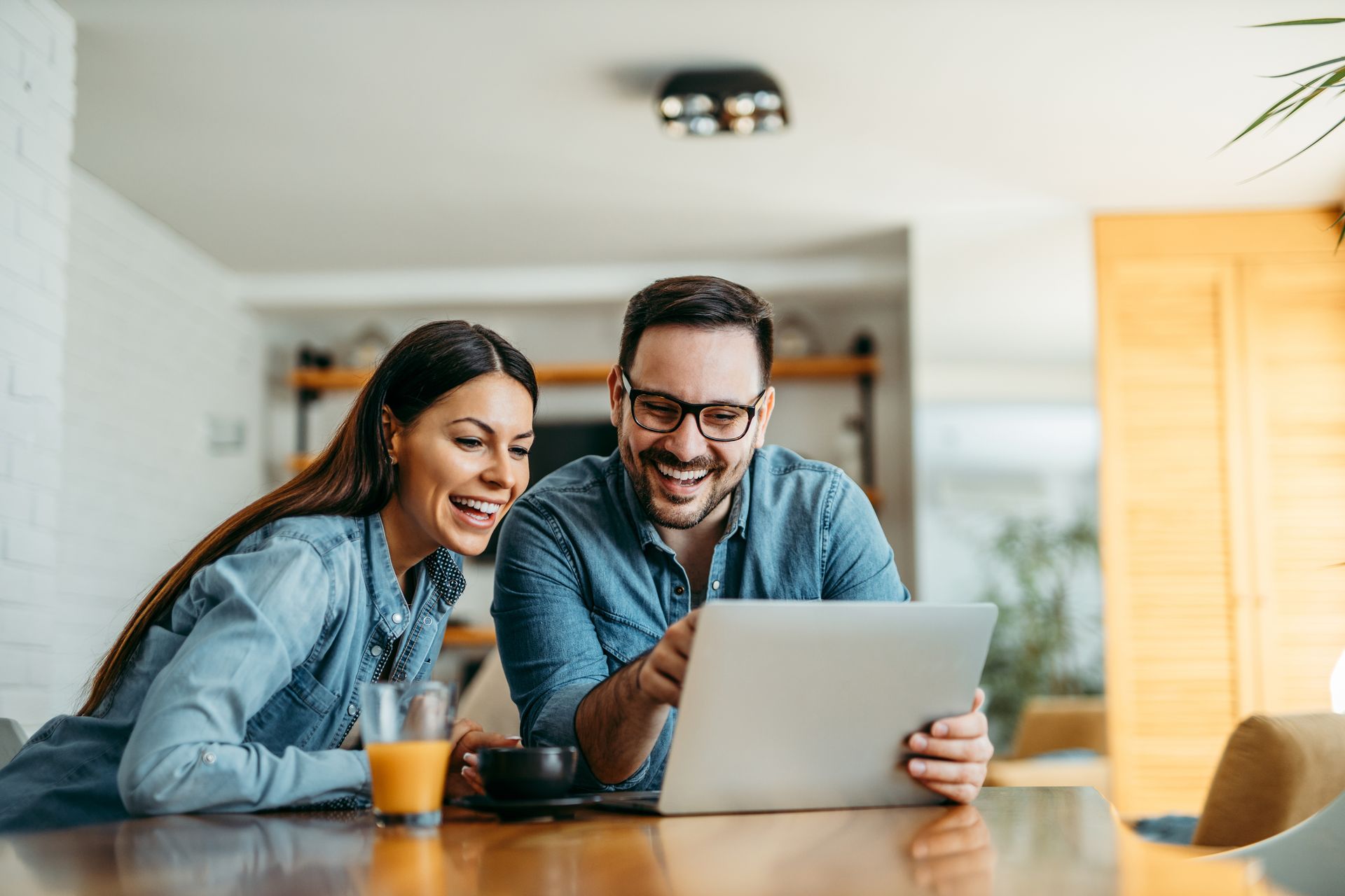 A man and a woman are sitting at a table looking at a laptop.