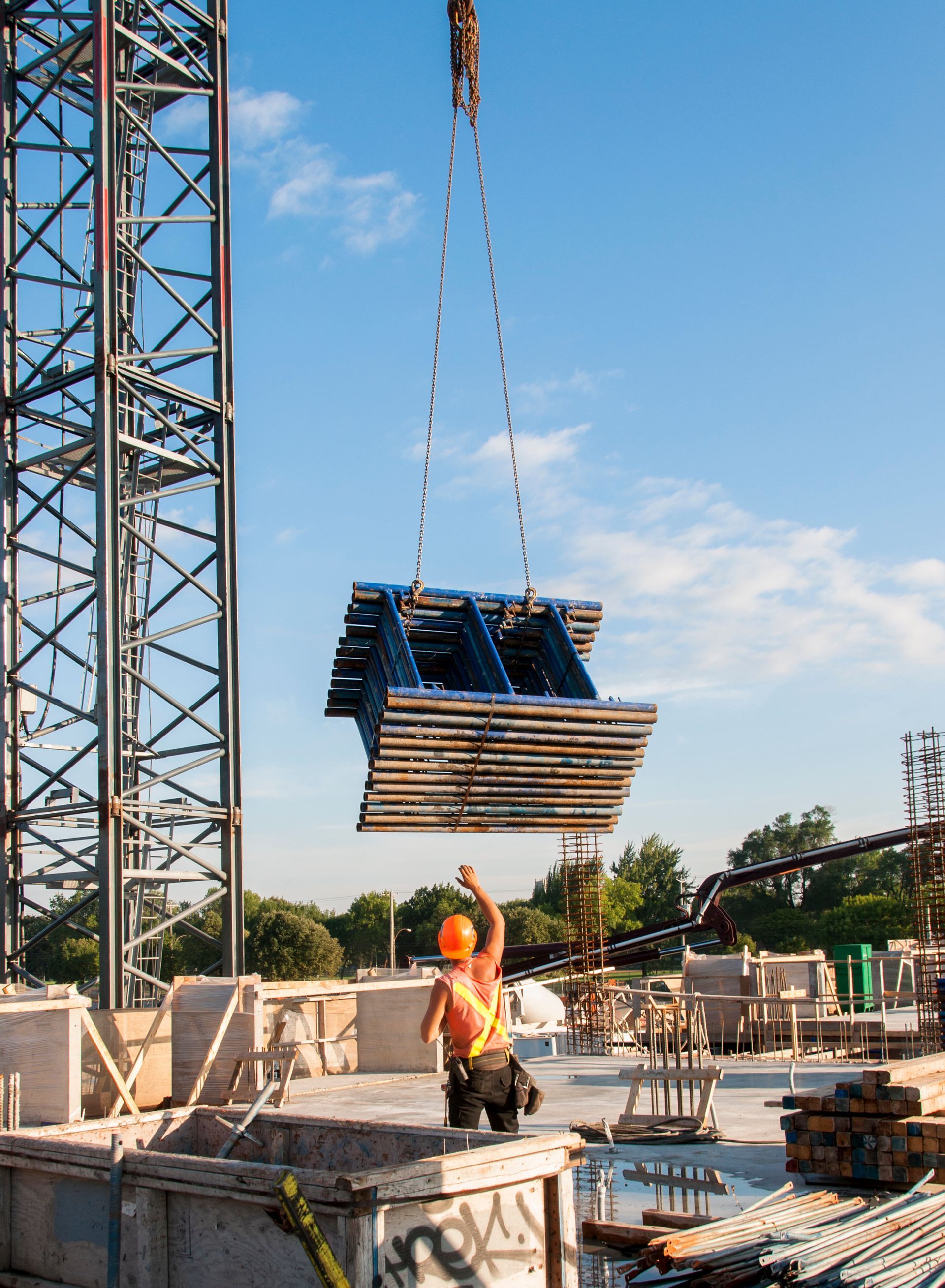 Construction worker guiding suspended metal structure with crane on a sunny day.