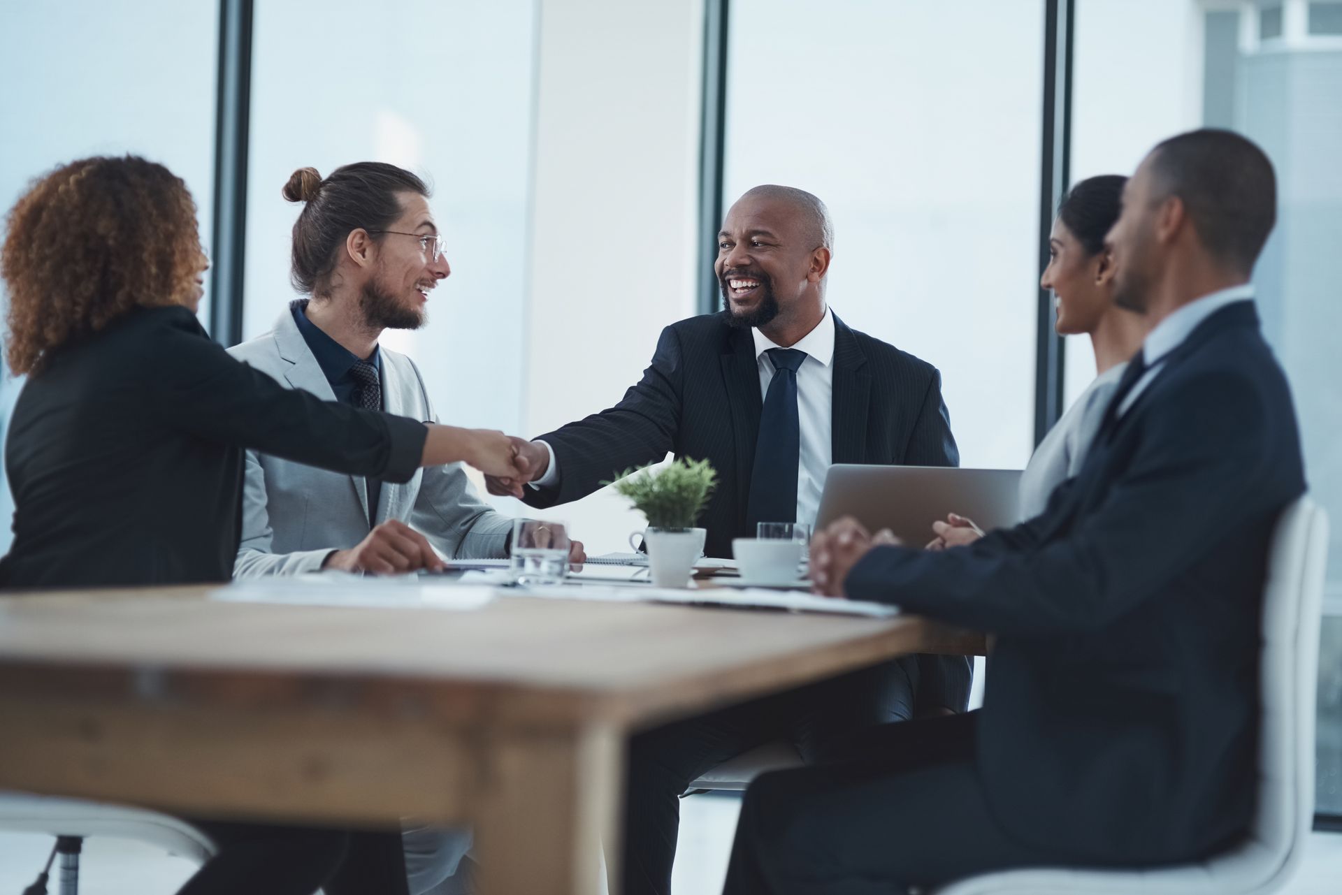 Business colleagues shaking hands at a table in an office, smiling.