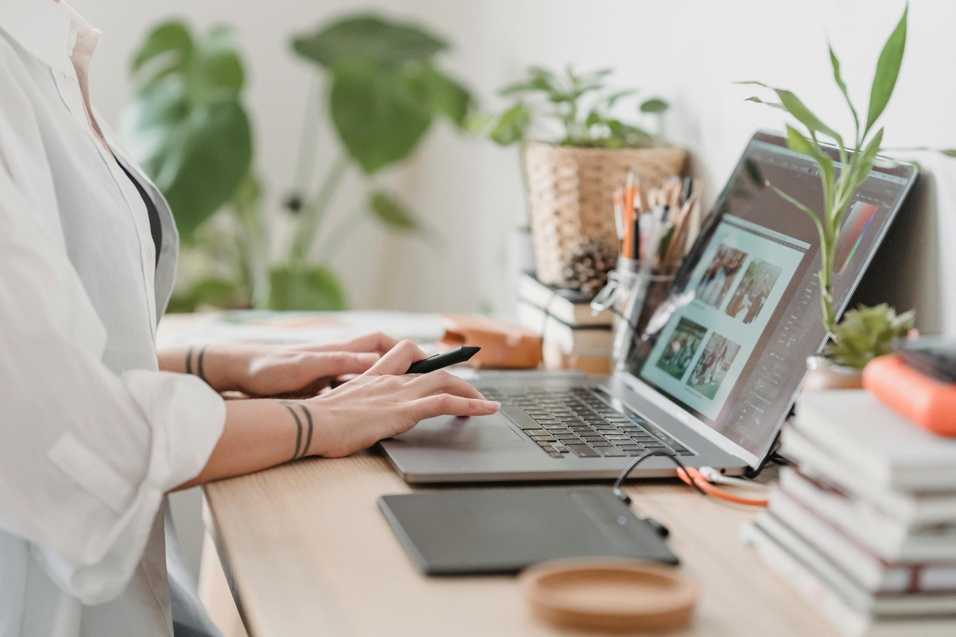 Person working on laptop, with desk setup including plants and tablet.