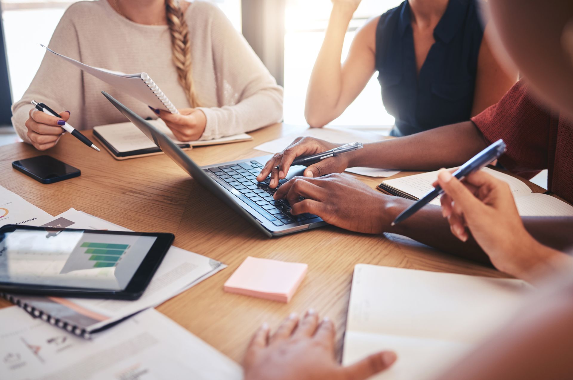 People working at a table with a laptop, tablet, and papers, collaborating and taking notes.