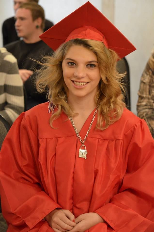 Person in red graduation gown and cap smiling, wearing a necklace.
