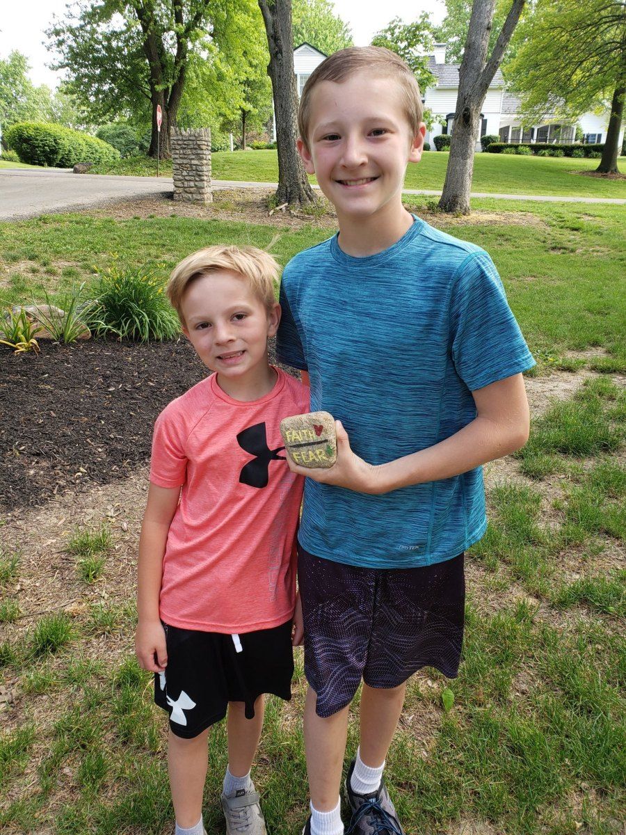 Two boys holding a small box outdoors; one wears blue shirt, the other wears a red shirt.