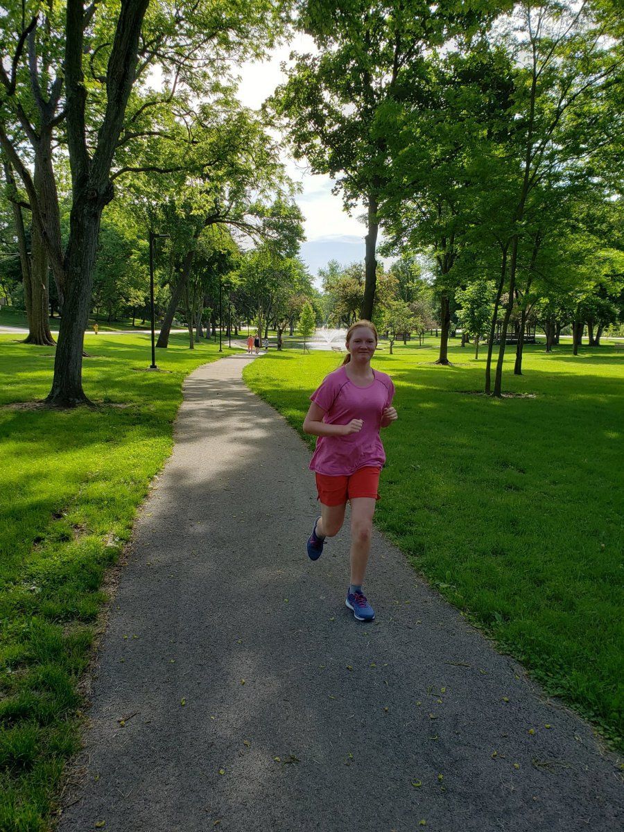 Woman jogging on a park path, surrounded by trees and green grass.