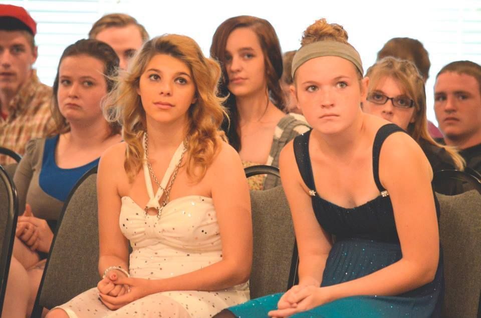 Group of people seated, some looking forward, in a room, attending an event.
