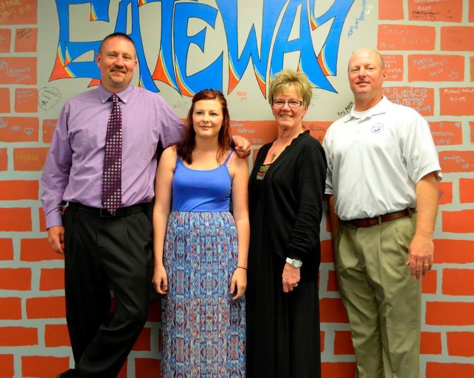 Four people pose in front of a brick wall with 