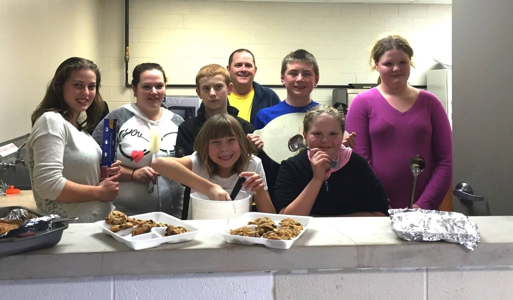 Group of people at a counter with baked goods, smiling.