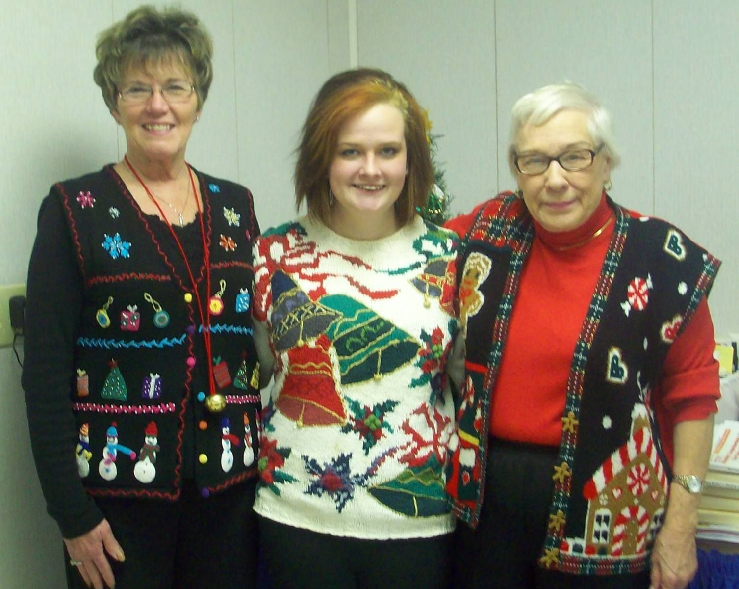 Three people in Christmas sweaters, posing indoors.