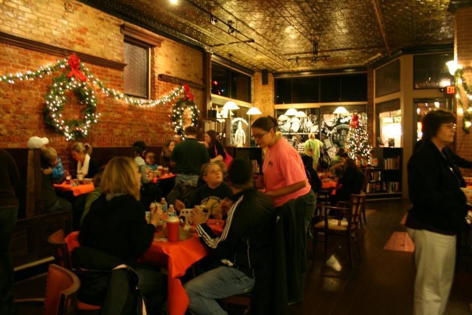 Restaurant interior with brick walls, tables set for dining, and holiday decorations; patrons and a server.