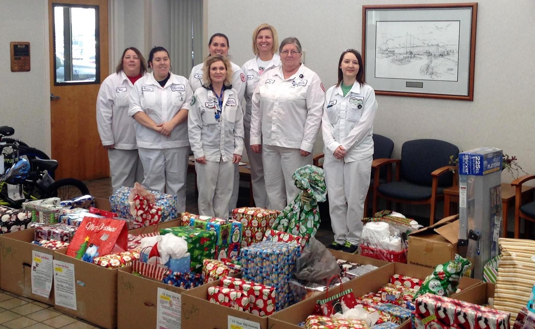 Group of people in white uniforms pose behind wrapped gifts, likely for a donation.