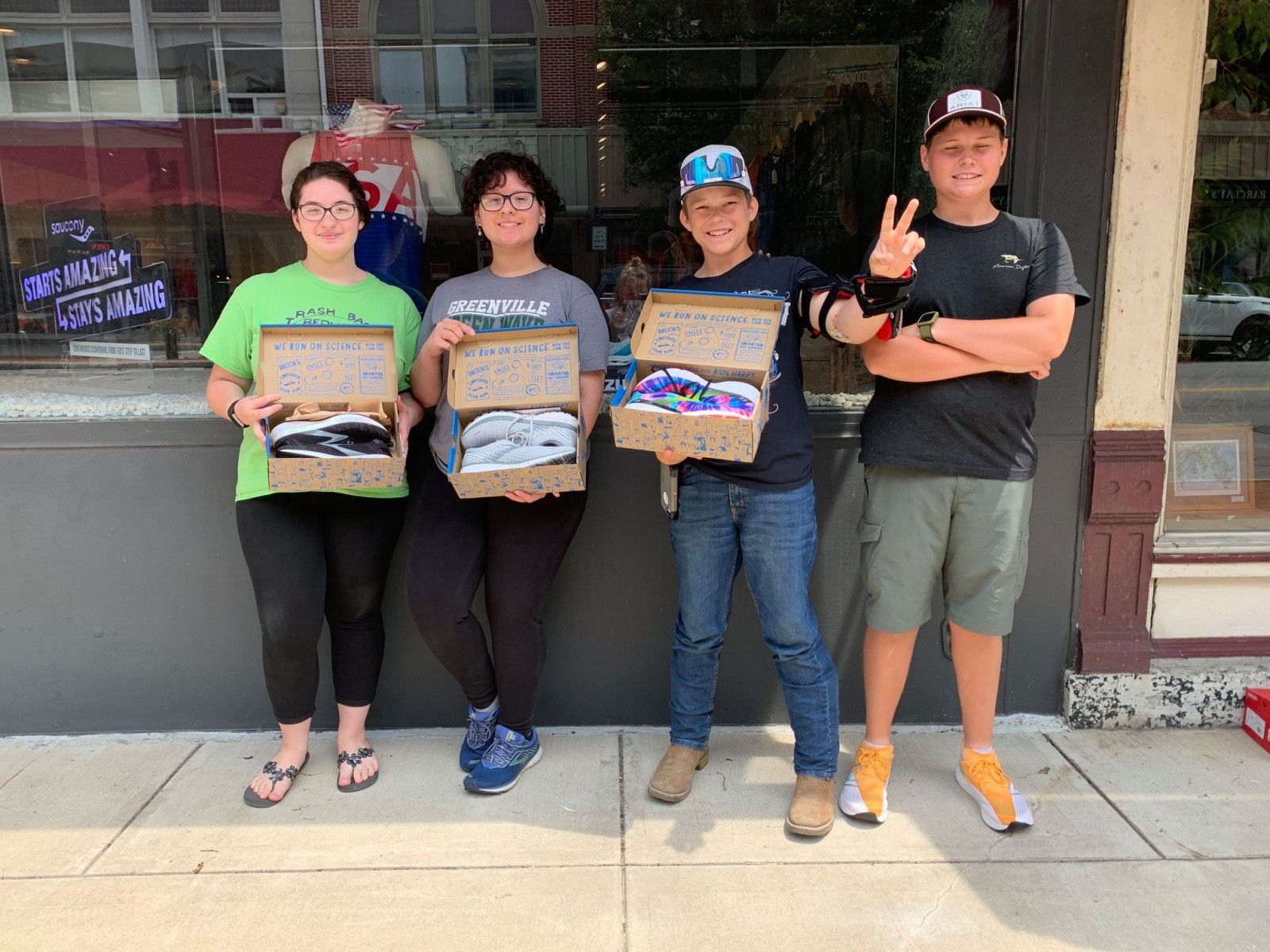 Four people holding shoeboxes filled with shoes in front of a storefront.