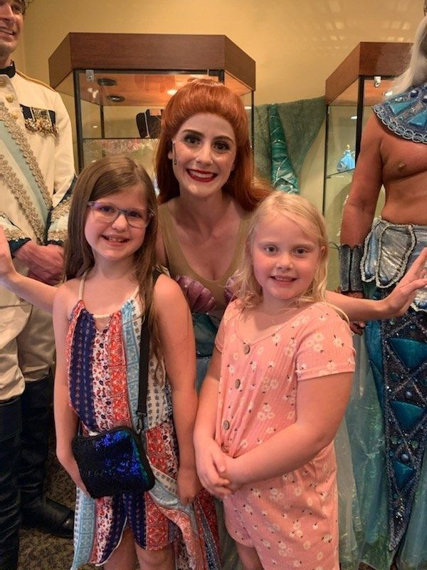 Two young girls pose with a woman in a costume, possibly a performance at a show.