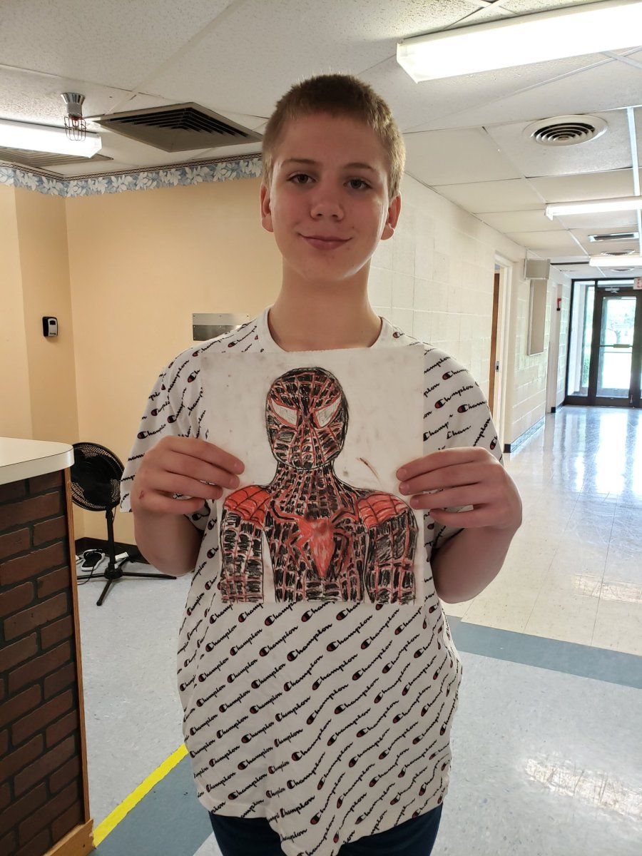 Boy holding a drawing of Spider-Man in a hallway. The drawing has red and black details.